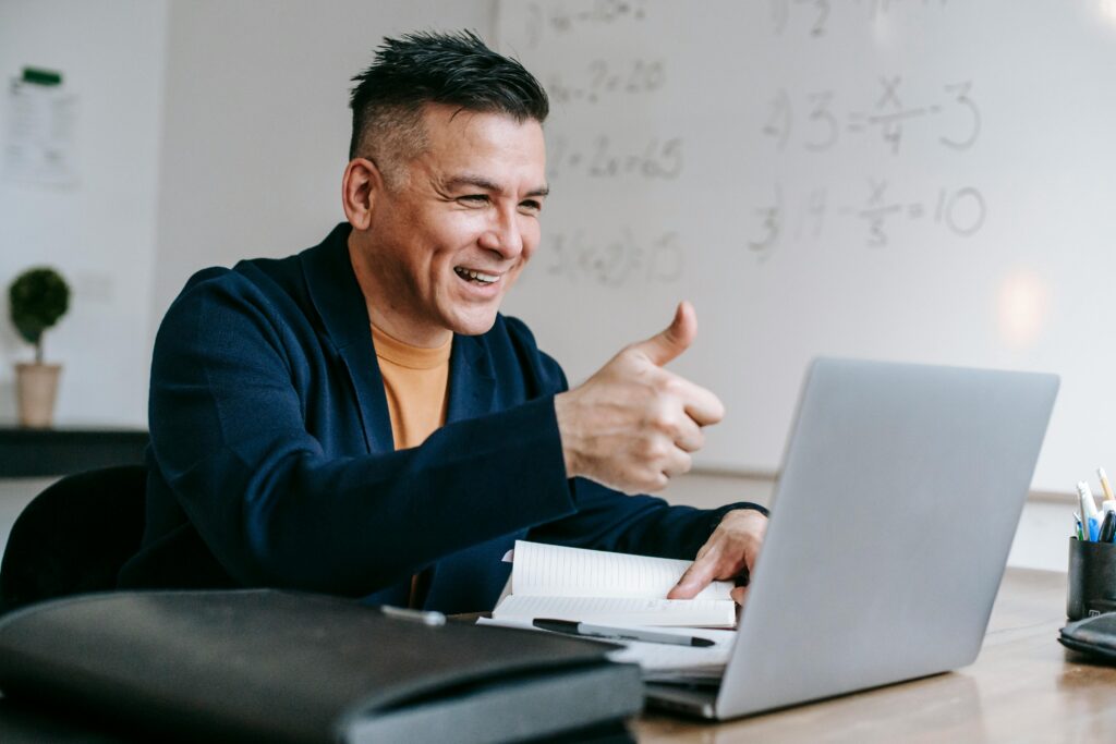 Happy man gives thumbs up while video conferencing from home office.